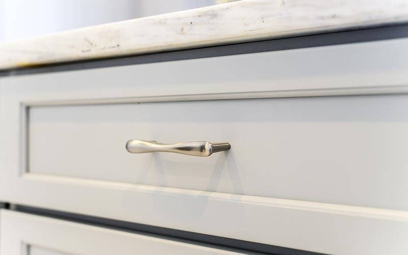 Close-up of a light gray shaker-style cabinet drawer with a sleek, metallic handle and a stone countertop above.