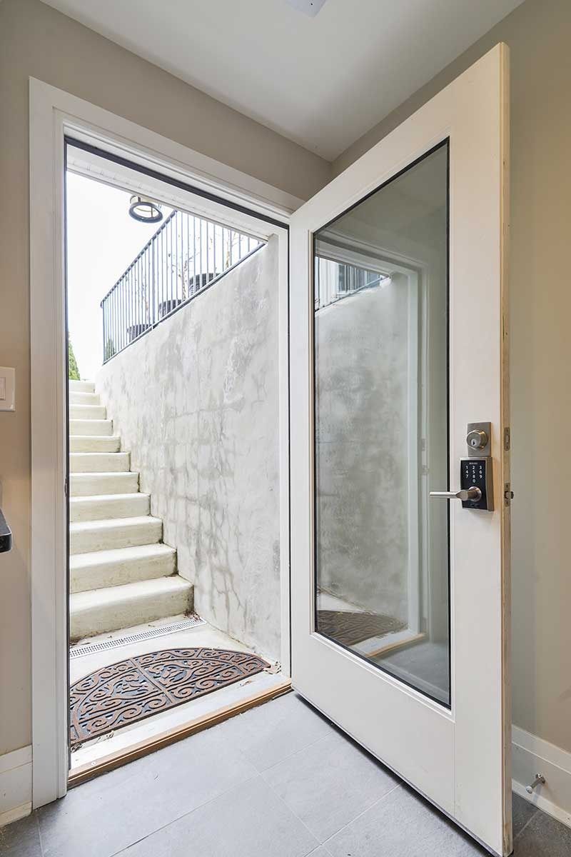 An open white door with a large glass panel reveals concrete stairs leading upward to an outdoor metal railing.