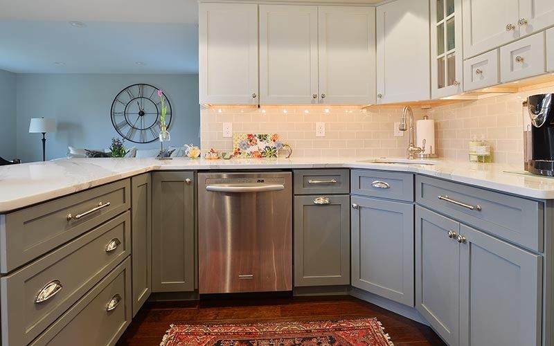 A kitchen with grey cabinets, stainless steel appliances, white countertops, and a patterned rug on a dark wood floor.