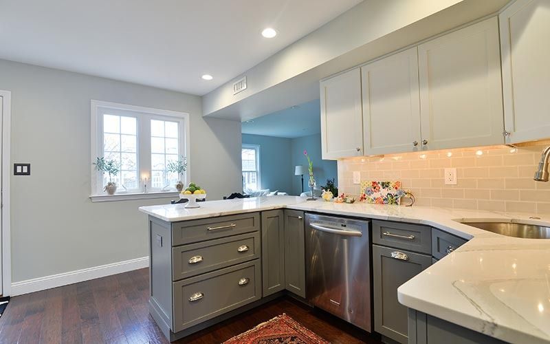 A modern kitchen with grey cabinets, light-colored countertops, stainless steel appliances, and wood flooring.