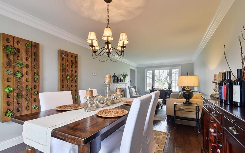 A wood dining table with white chairs sits under a chandelier, with vertical succulent planters on the side wall.