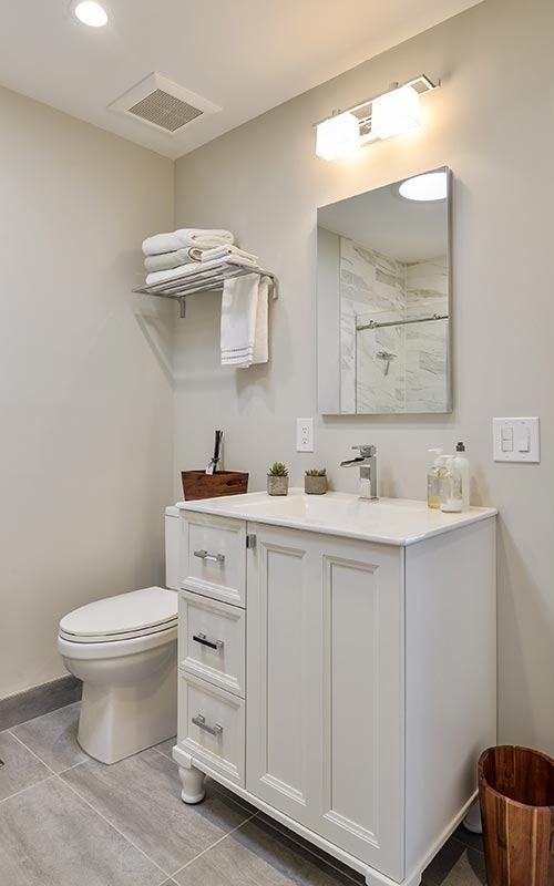 Modern bathroom with a white vanity, a rectangular mirror, a toilet, a wall-mounted towel rack, and grey tile floors.
