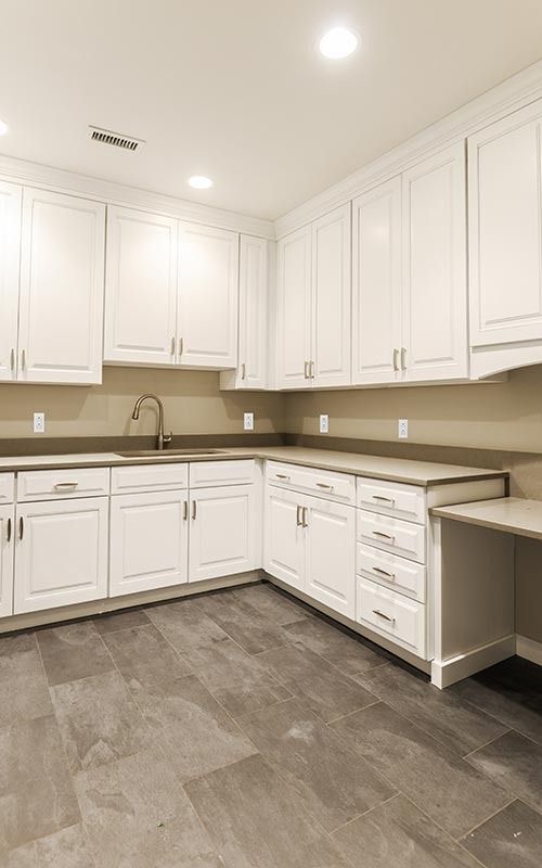 Modern kitchen featuring white shaker cabinets, light gray countertops, and large format gray floor tiles.