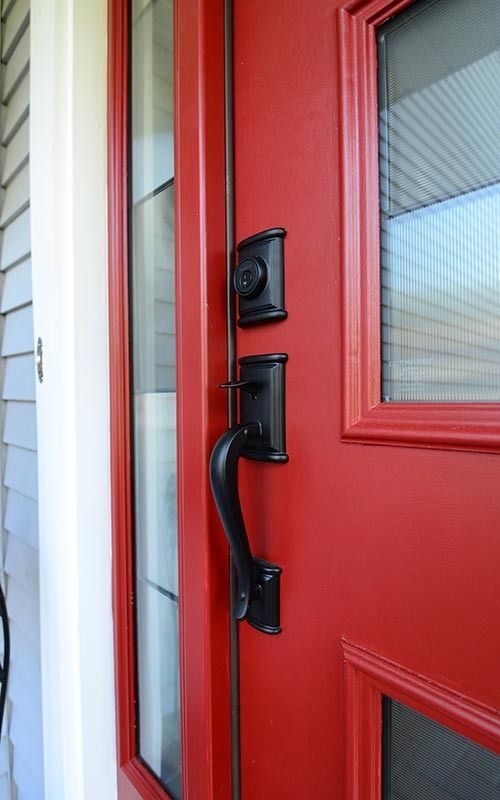 A matte black modern door handle and deadbolt lock set on a vibrant red front door with glass side panels.