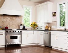 A bright kitchen featuring white cabinets, stainless steel appliances, a range hood, and a bouquet of sunflowers.