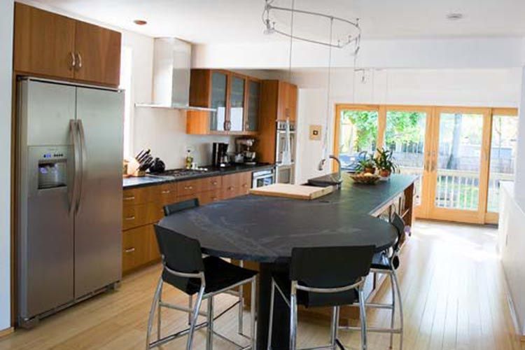 A modern kitchen with wooden cabinets, stainless steel appliances, a black oval island, and bar stools.