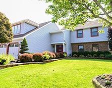 A two-story suburban house with light blue siding, a partial brick facade, and a neatly manicured lawn.