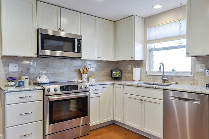 A modern kitchen with off-white cabinets, stainless steel appliances, light granite countertops, and wood-look flooring.