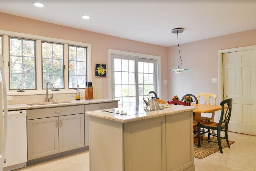 A kitchen with grey cabinets, a center island, a dining table with chairs, and sliding glass doors under recessed lights.