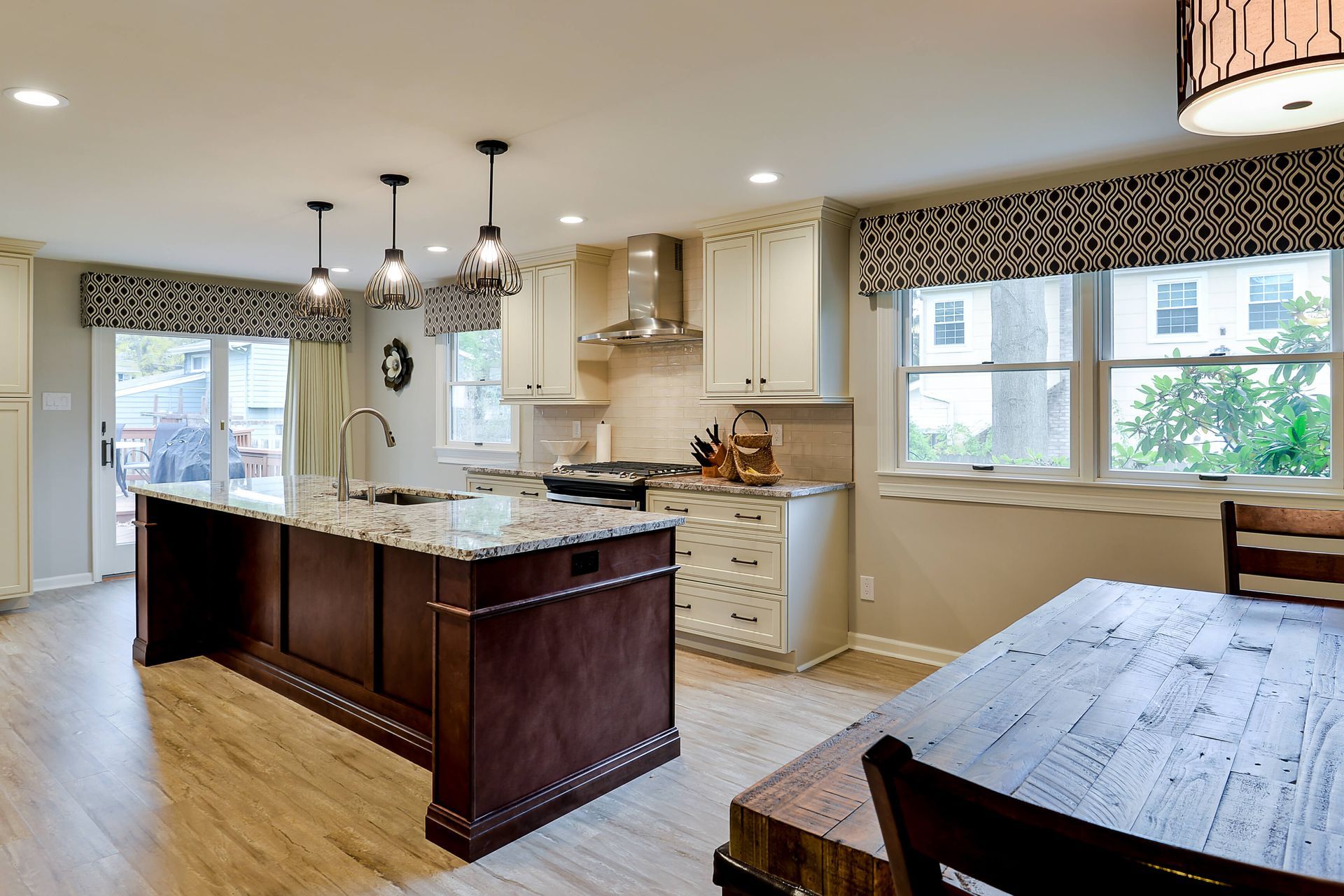 A bright, modern kitchen featuring a dark wood island with granite countertops, cream cabinets, and a rustic wood table.