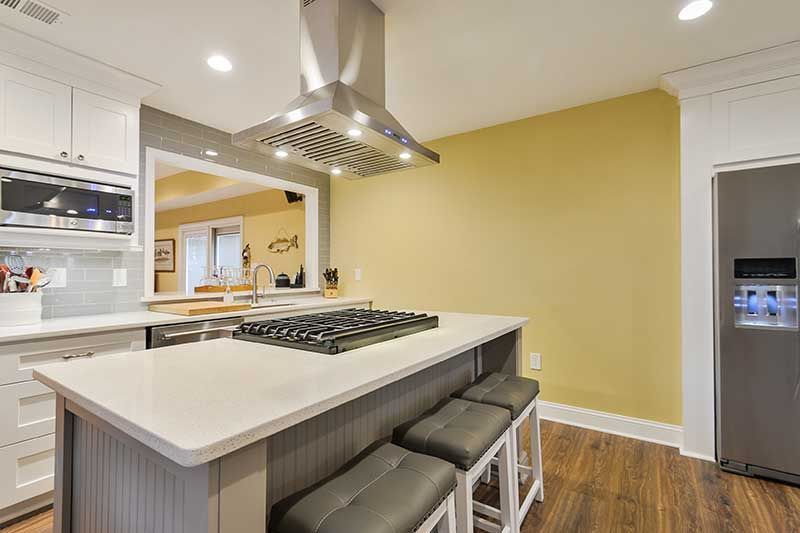 Modern kitchen with a gray island, a stovetop and vent hood, white cabinets, stainless steel fridge, and yellow walls.