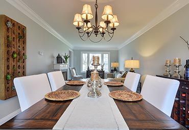 A dining room with a long wooden table, white chairs, a centerpiece, and a chandelier in an elegant, neutral-toned room.