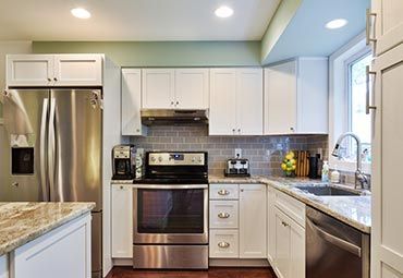 A kitchen with white cabinets, stainless steel appliances, granite countertops, and a grey subway tile backsplash.