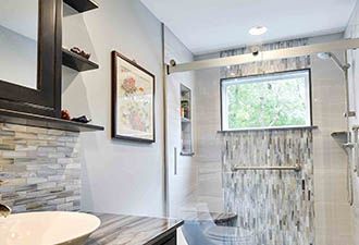 A bathroom features a vanity with a vessel sink, a shower with sliding glass doors, a window, and decorative wall tiles.