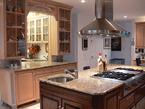 A kitchen with a large island containing a gas stovetop and sink, featuring wooden cabinets and granite countertops.