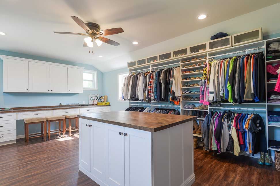 A large walk-in closet featuring white cabinetry, a central wooden island, extensive hanging storage, and wood floors.