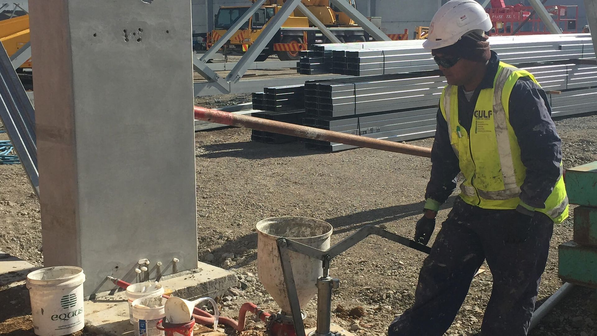 Construction worker wearing safety gear pouring concrete at a construction site.