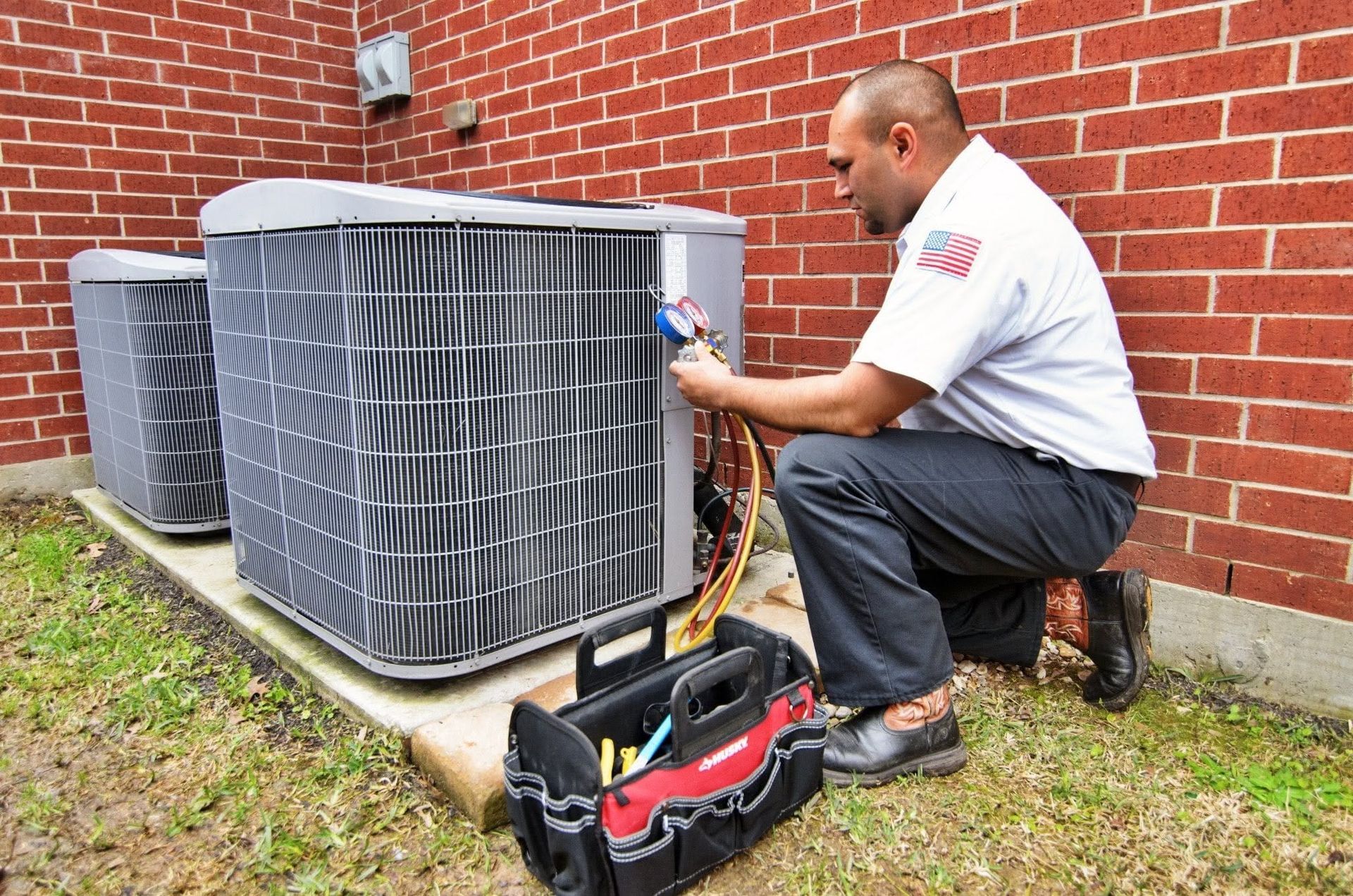 HVAC technician servicing outdoor air conditioner units beside a brick wall