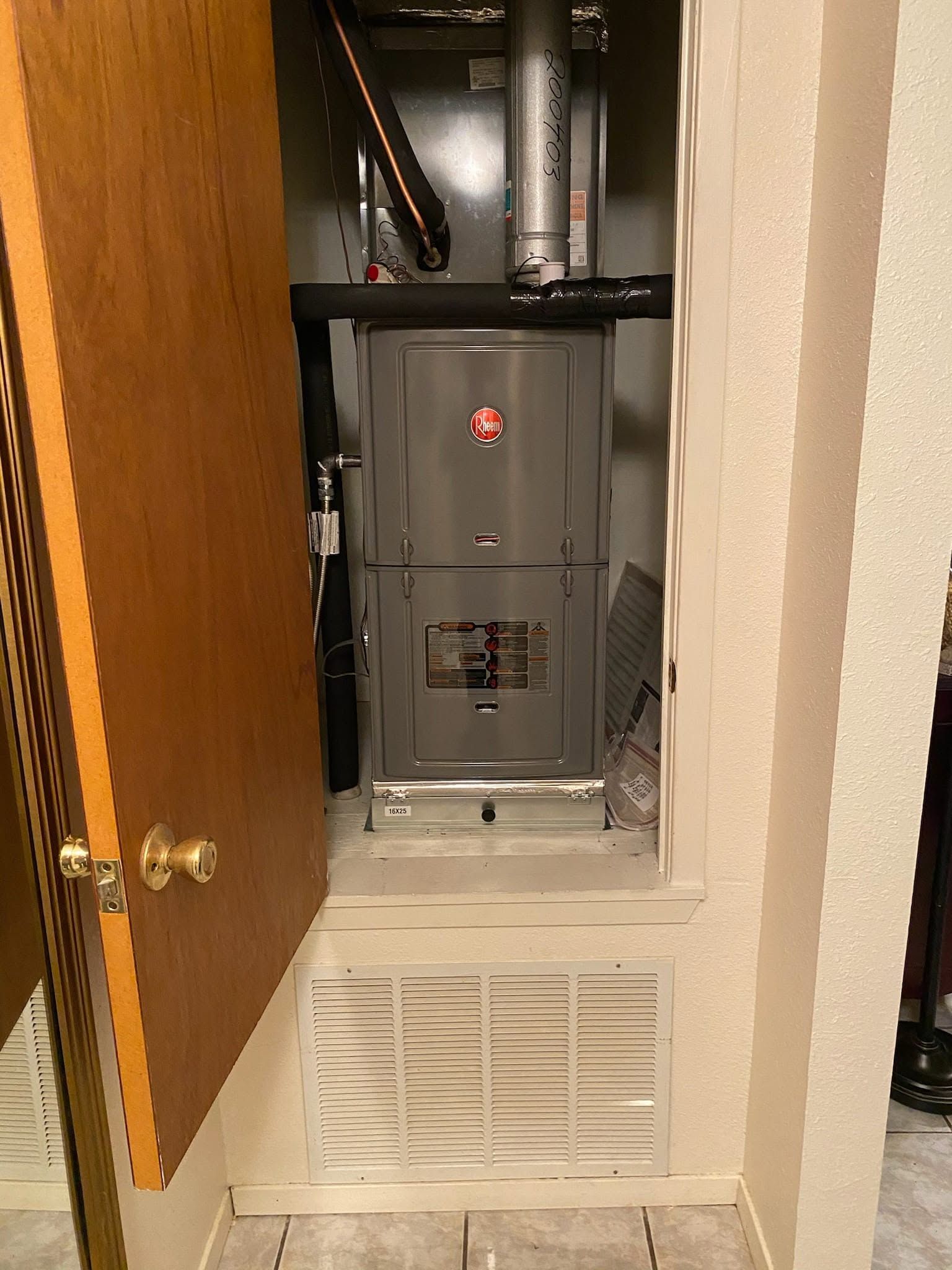 Open closet with gray furnace and air vent behind a partly open wooden door.