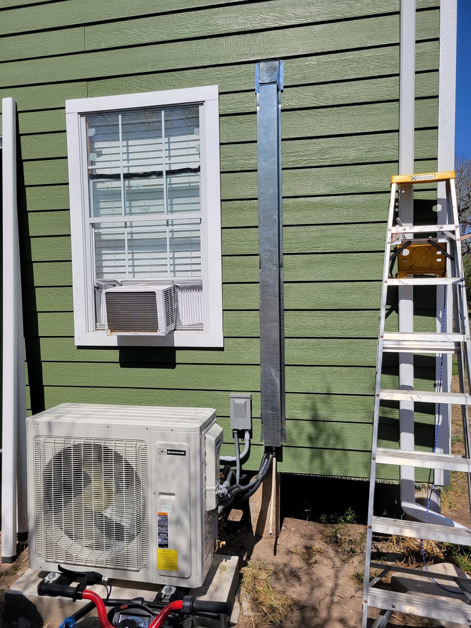 Exterior wall with window, HVAC unit, and ladder beside a green-sided house