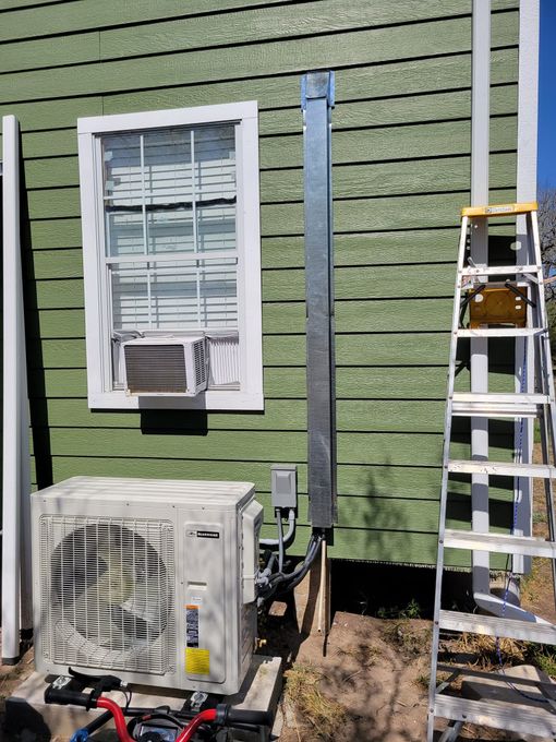 Exterior wall with window, HVAC unit, and ladder beside a green-sided house