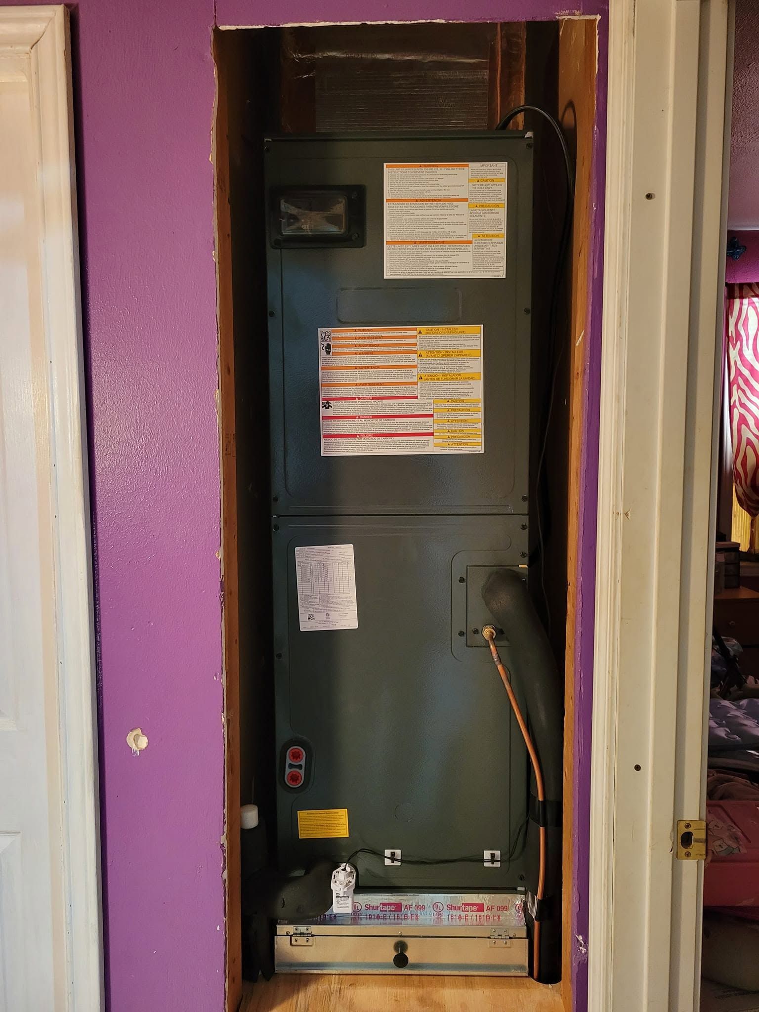 Open electrical breaker panel in a purple wall alcove with warning labels and conduit.