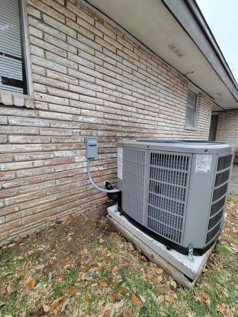 Outdoor HVAC unit beside a brick wall with conduit and fallen leaves on the ground