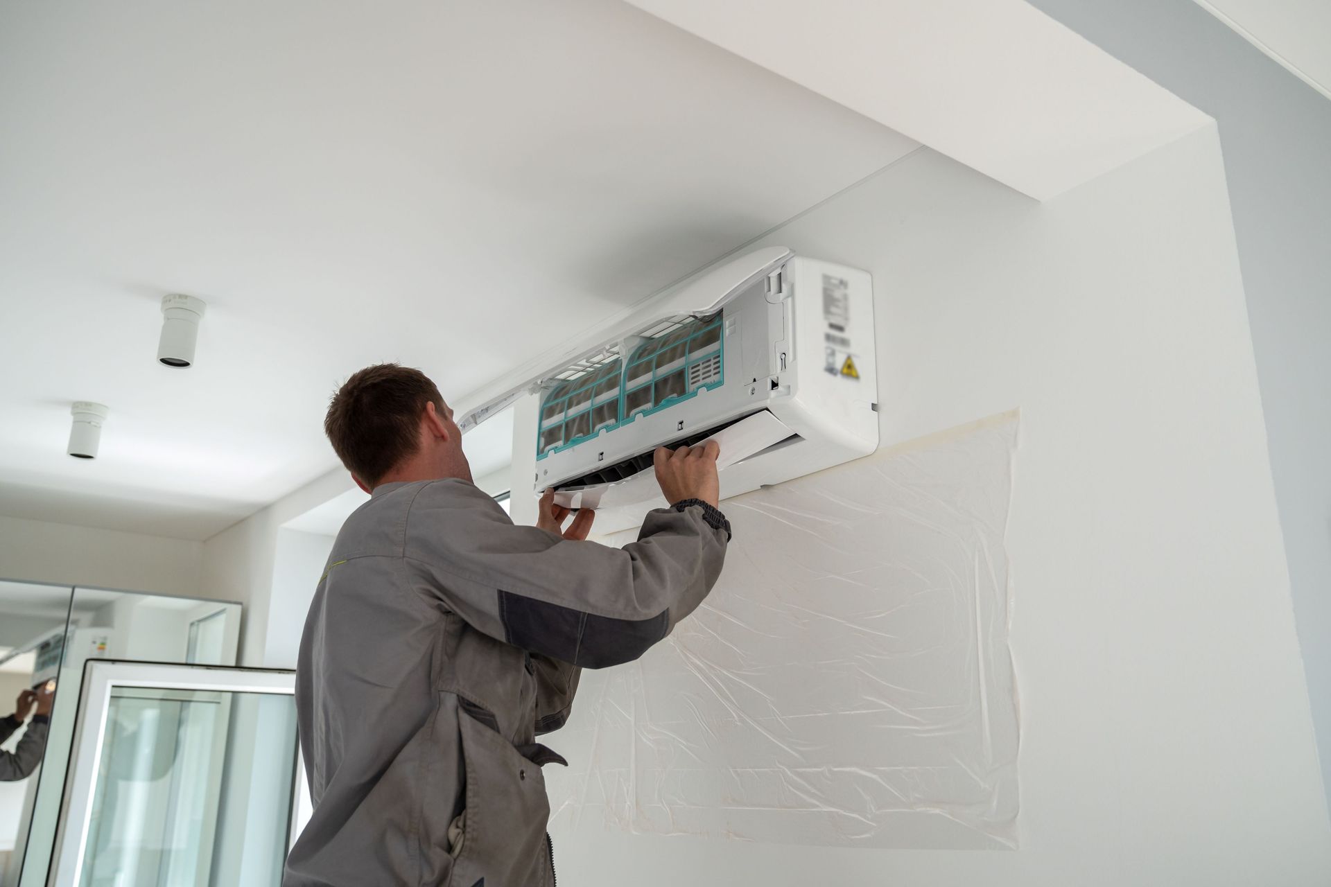 Technician installing a wall-mounted air conditioner in a white room