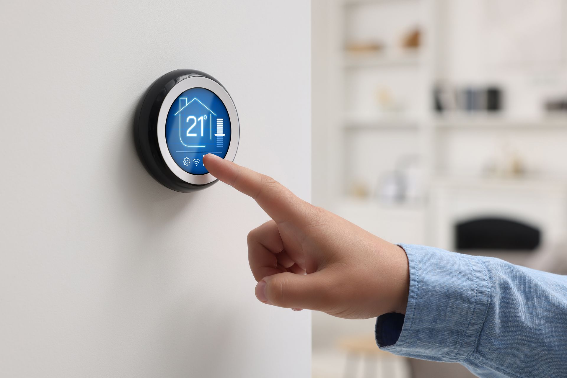 Hand adjusting a blue smart thermostat on a wall