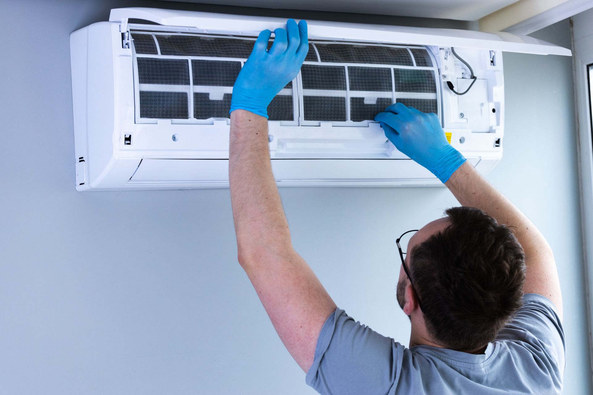 Technician cleaning a wall-mounted air conditioner with blue gloves