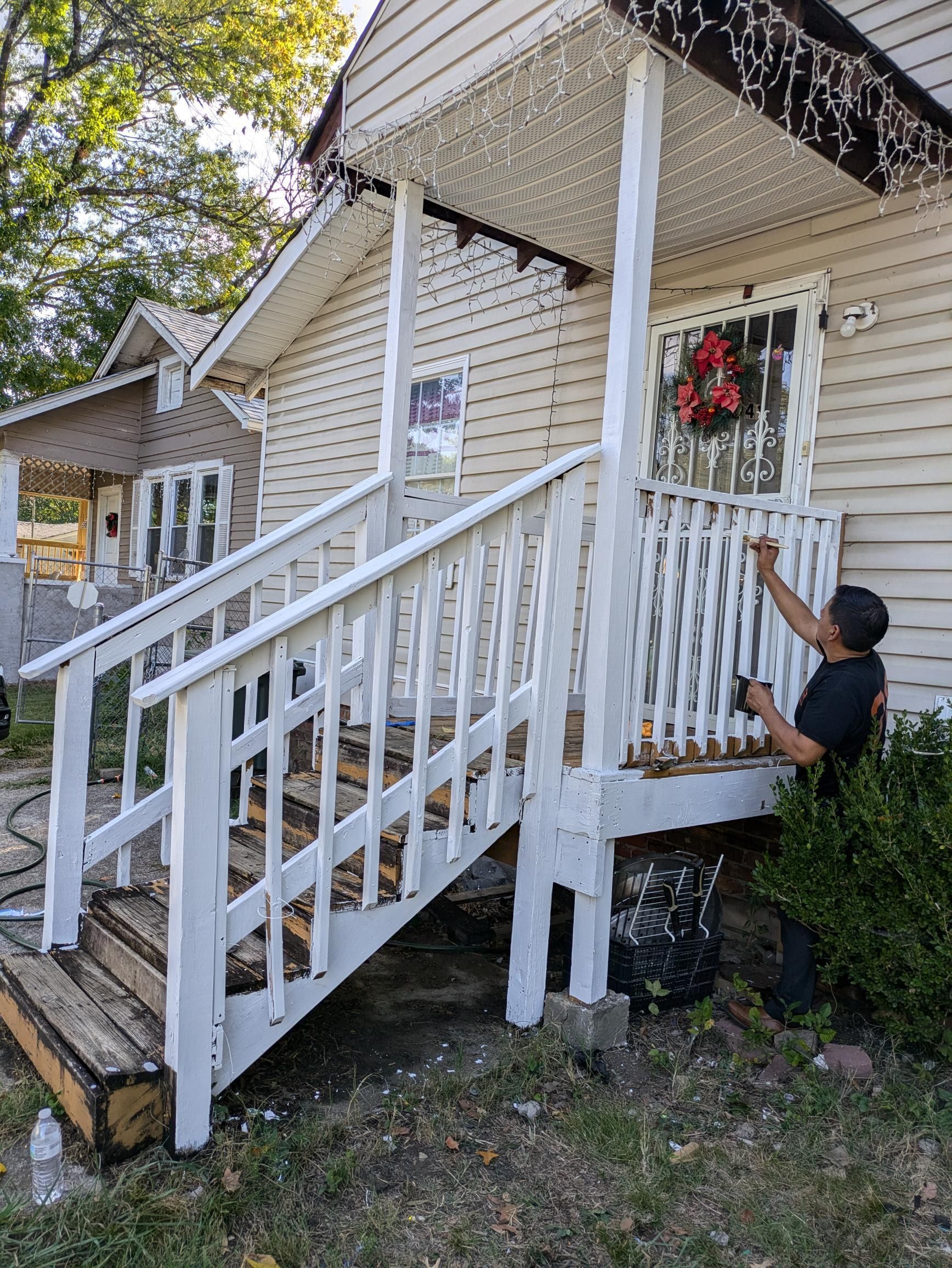 Person painting a white porch railing and stairs of a house with white siding.