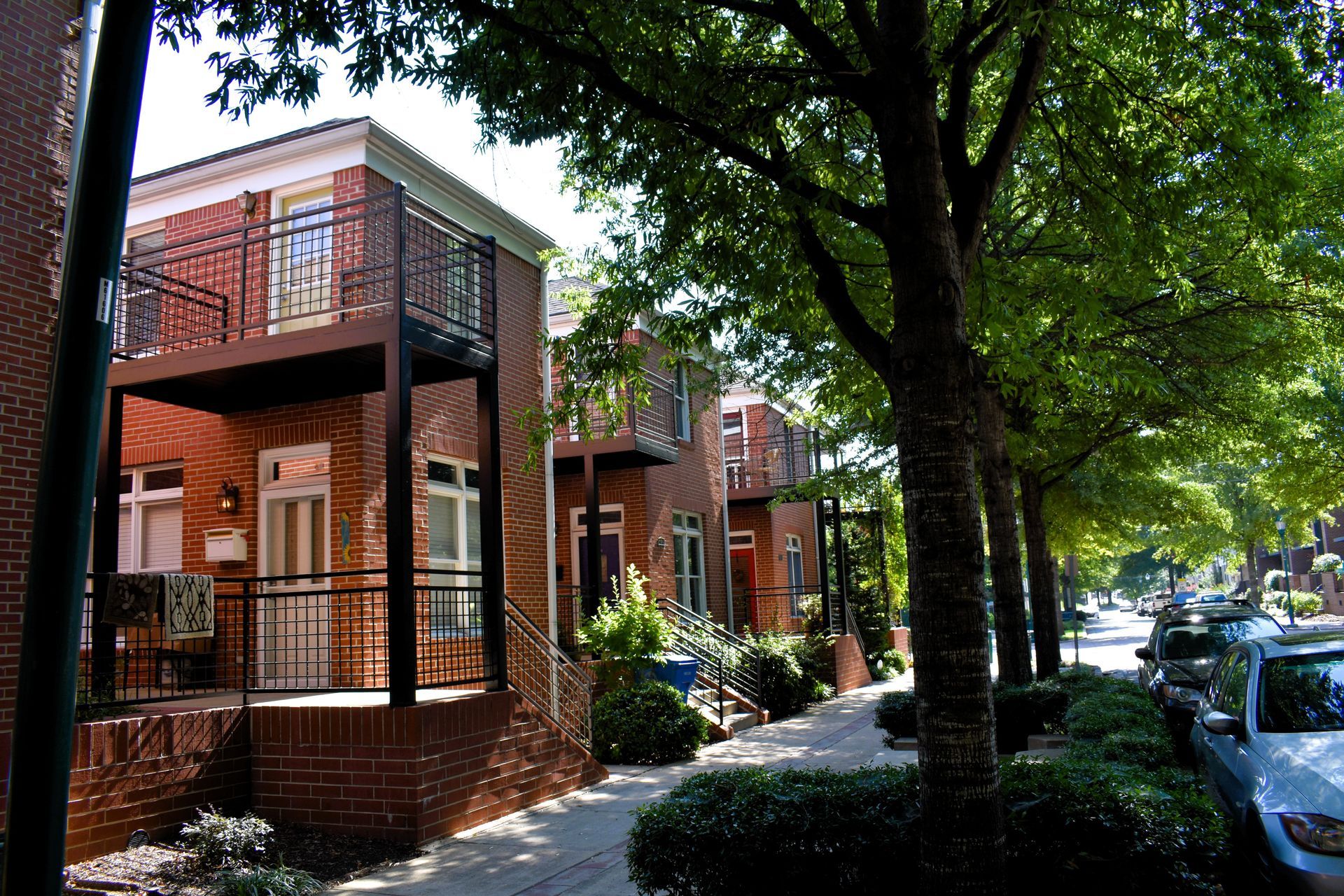 Brick townhouses with balconies and a tree-lined street with parked cars.