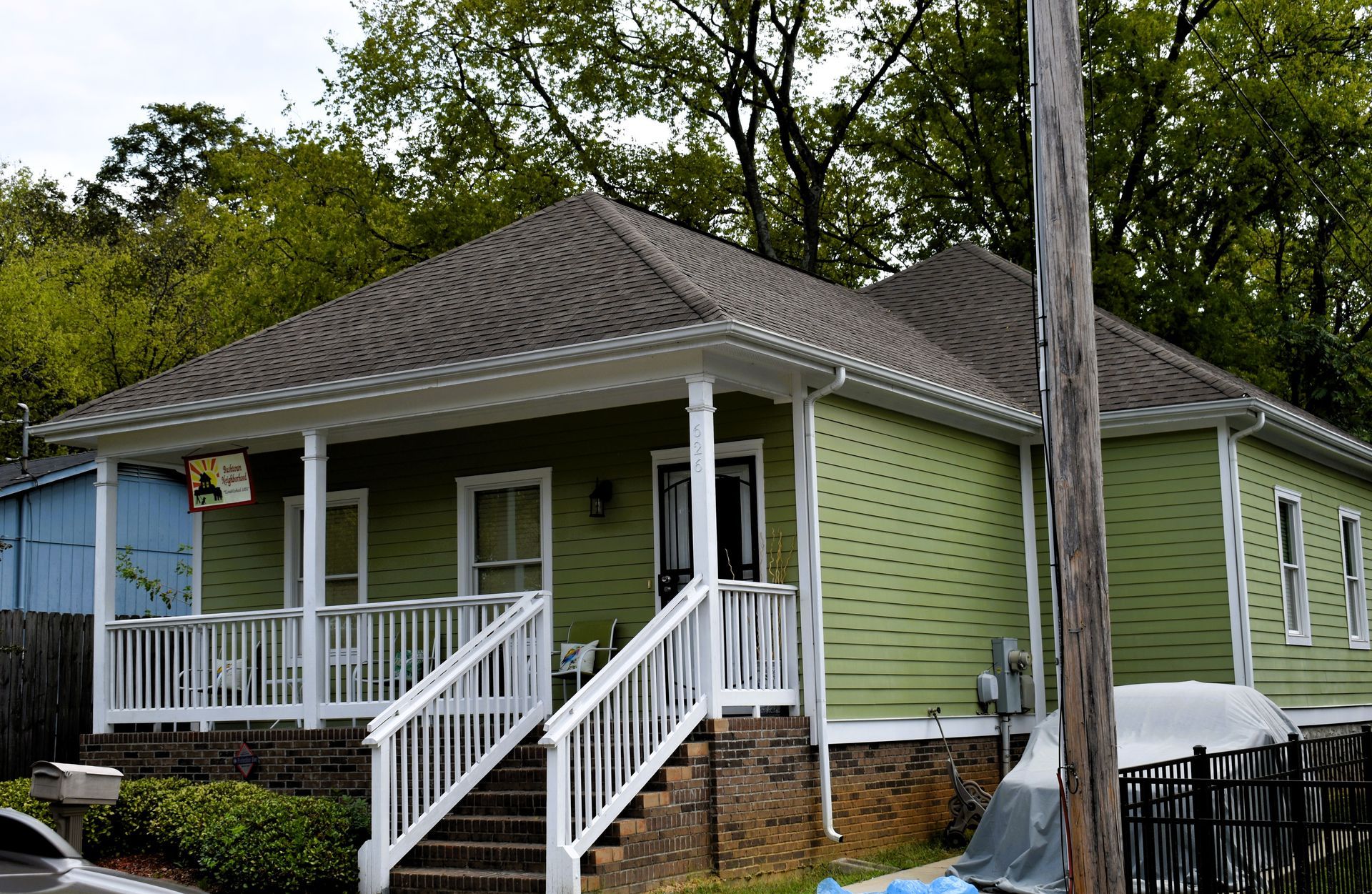 Green house with white porch and stairs, brown roof, and utility pole in front.