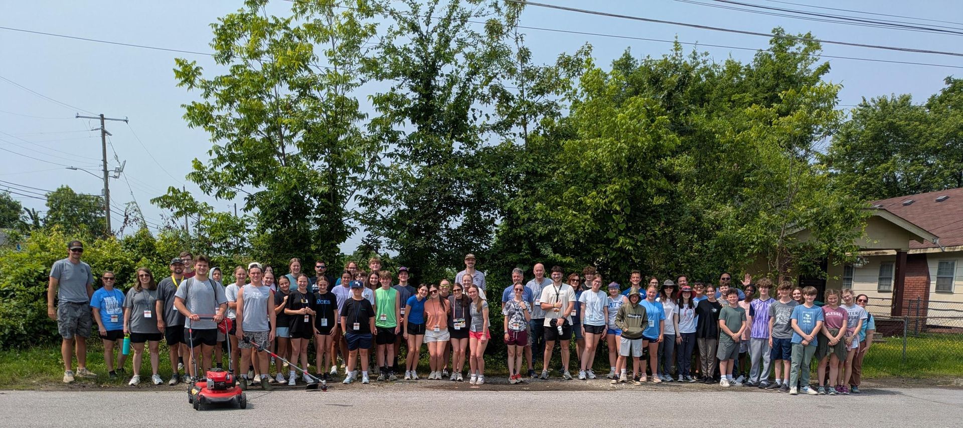 A group of people standing outside, possibly a sports team. Large green trees in the background.