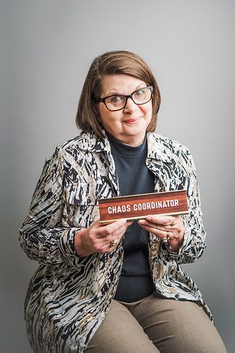 A woman wearing glasses and a patterned jacket holds a sign that reads 
