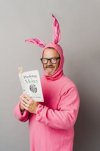 A man in a pink bunny costume and glasses reads a book titled 