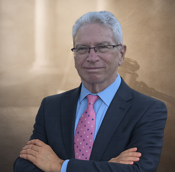 Professional portrait of a person in a suit and tie, arms crossed, in front of bookshelves and a scale of justice.