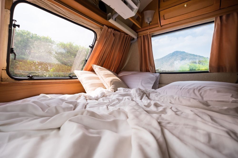 Bed inside a camper with rumpled white sheets, pillows, and views through the windows. — The Caravan Clinic in South Murwillumbah, NSW
