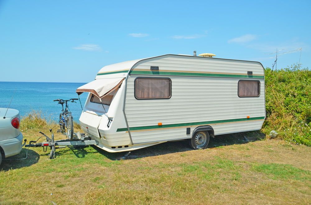 Caravan parked on grassy cliff overlooking the ocean, attached to a car. — The Caravan Clinic in South Murwillumbah, NSW