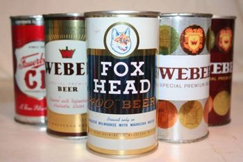 Assorted beer cans lined up on a table, including a central Fox Head beer can.