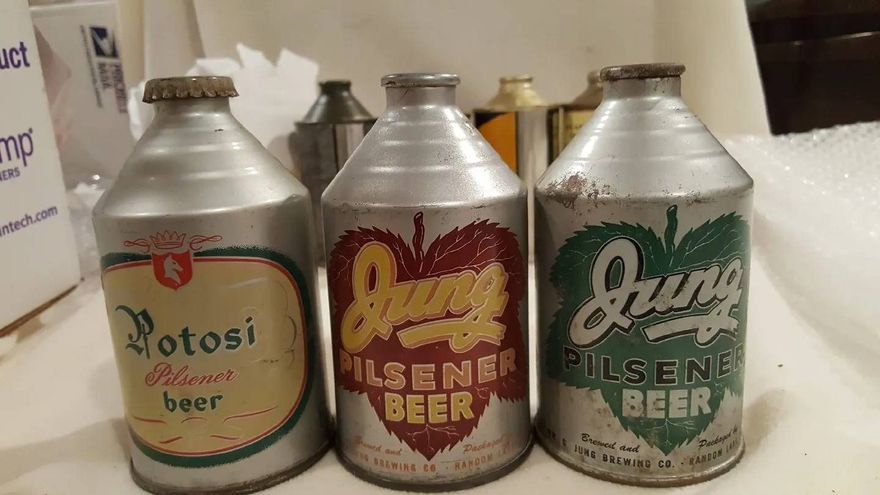 Three aluminum beer cans with vintage labels on a store shelf.