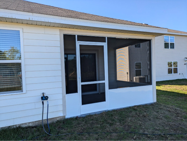 A white-framed screened porch attached to a white house with a clear blue sky in the background.