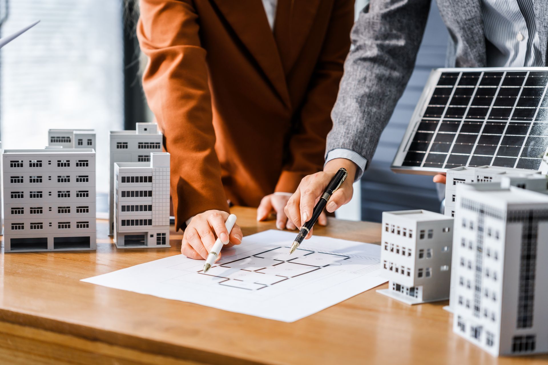 Deux personnes discutent d'un plan avec des bâtiments, un panneau solaire, une table, suggérant une planification urbaine.