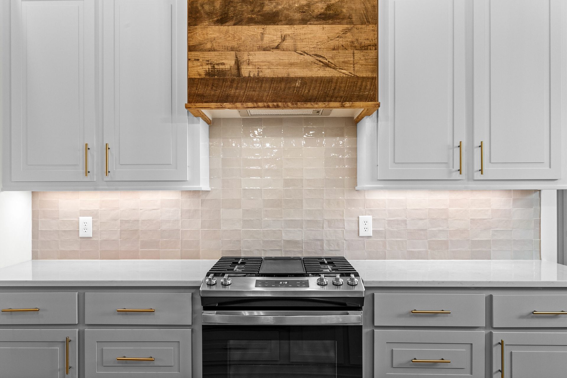 Modern kitchen with gray cabinets, white backsplash, and a stainless steel stove centered beneath a woven hood.