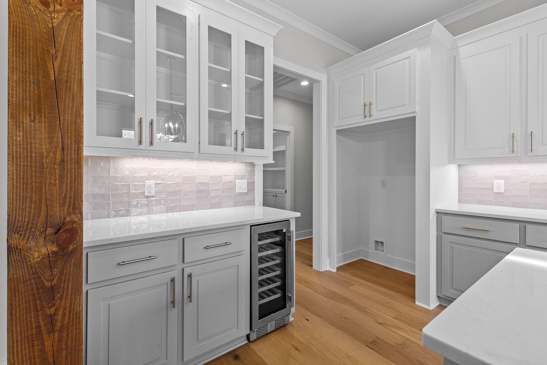Bright white modern kitchen with glass-front cabinets, wood floor, and wine fridge