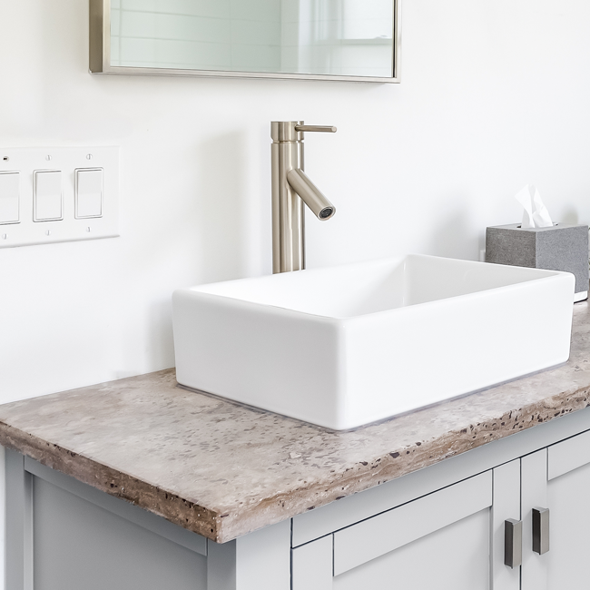 Modern bathroom vanity with a white vessel sink and brushed metal faucet on a rustic countertop