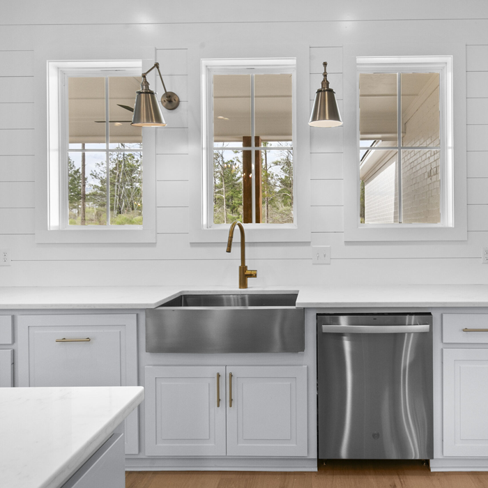 Bright white kitchen with three windows, pendant lights, farmhouse sink, and stainless dishwasher