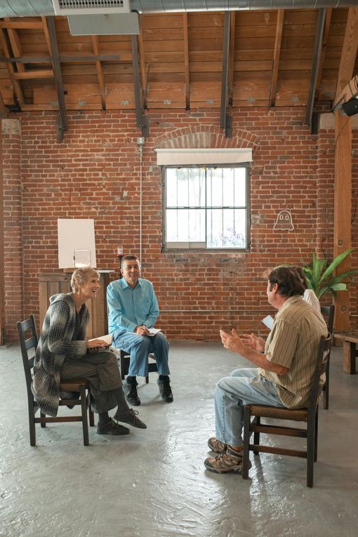 A group of people are sitting in chairs in a room with a brick wall.