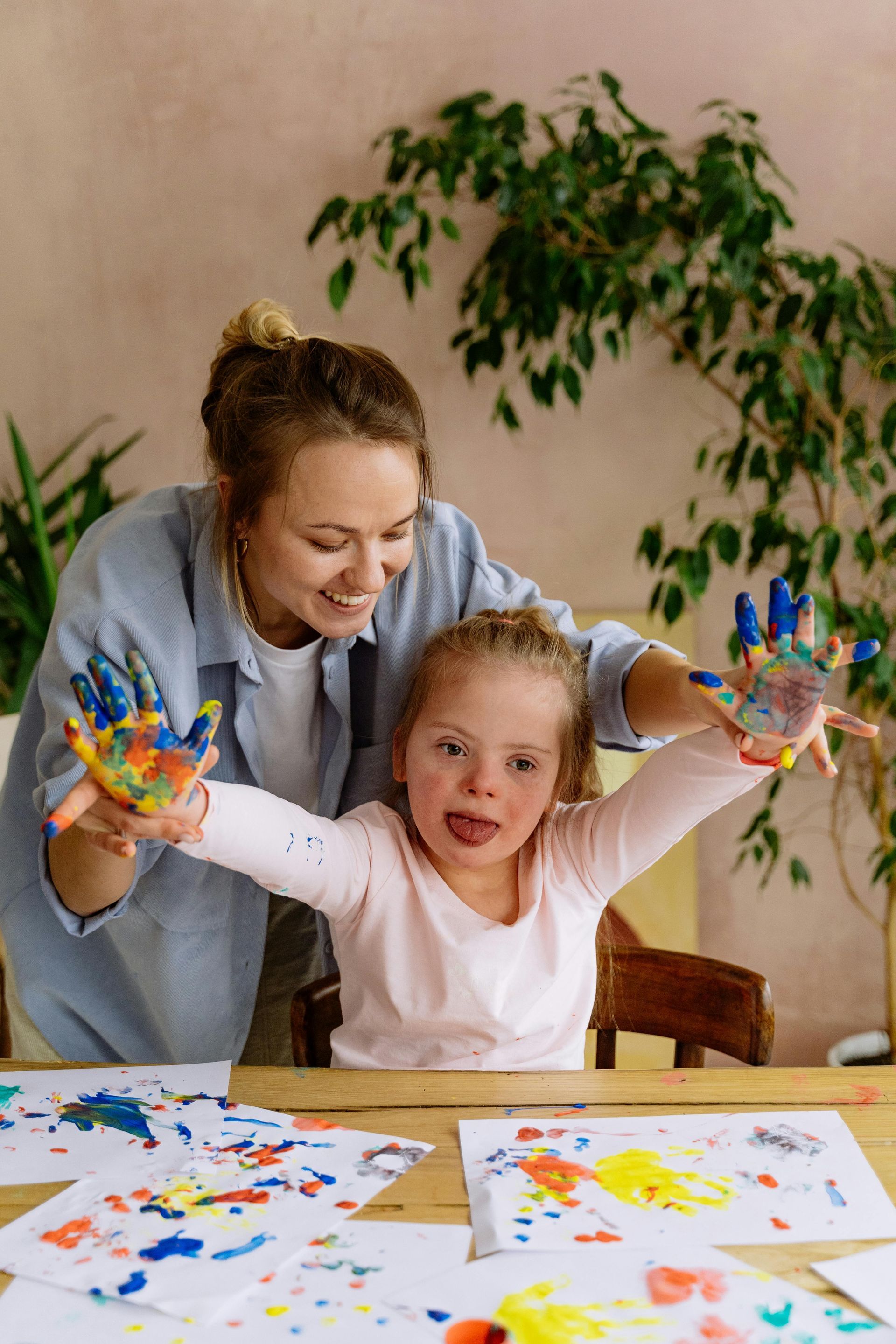 A woman and a little girl are sitting at a table with their hands painted.