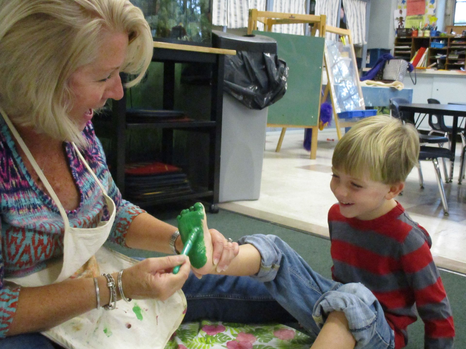 Woman painting a child’s foot green while a boy watches in an art studio